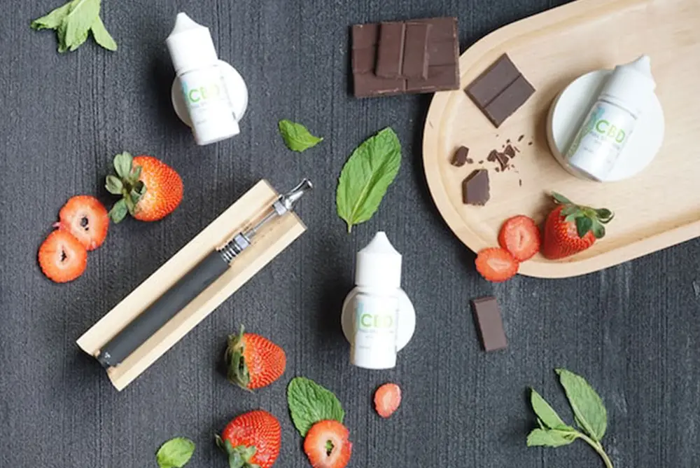 CBD oil, chocolate, strawberries, and a vape pen on a table