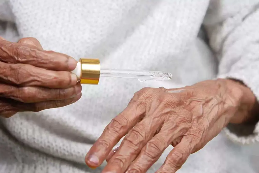 an elderly woman uses a dropper to apply CBD oil to her hand