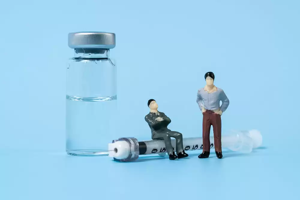 Two toy figurines next to a syringe and a tiny glass vial.