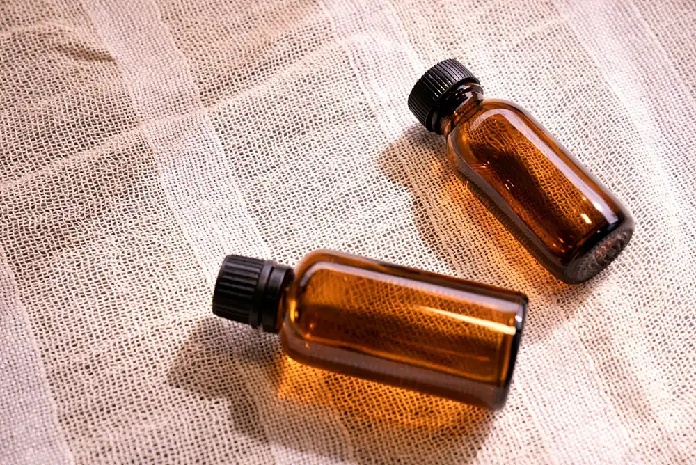 Two small amber glass bottles with black caps lying on a textured fabric surface.