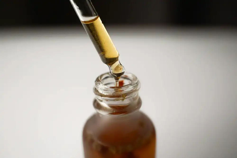 Glass dropper dispensing amber liquid into a small glass bottle.