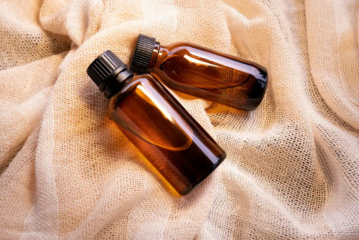 Essential Oil Packaging: Tips and Trends | Acme Vial two amber glass bottles lay on a natural textured cloth backdrop